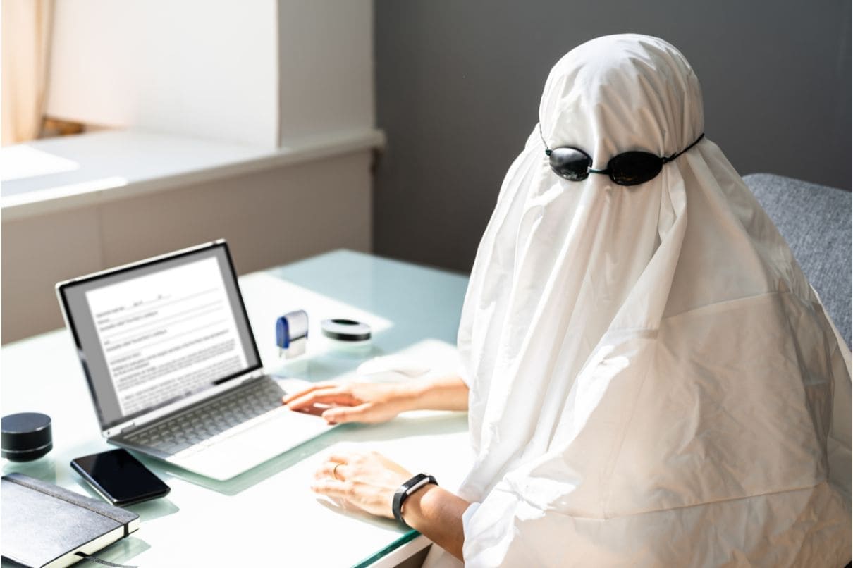 A person wearing a white sheet, glasses, and using a laptop.